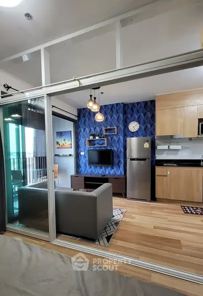 Modern open-plan living room with stylish decor and kitchen area, featuring a sleek fridge and contemporary lighting.