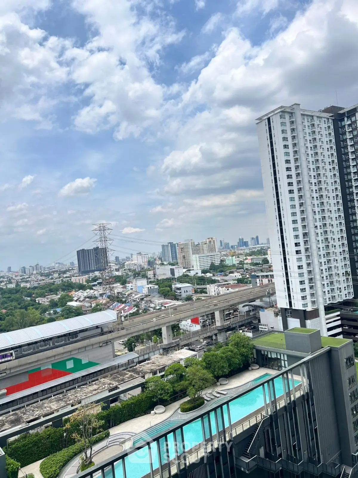Stunning cityscape view from high-rise building with pool and lush greenery.