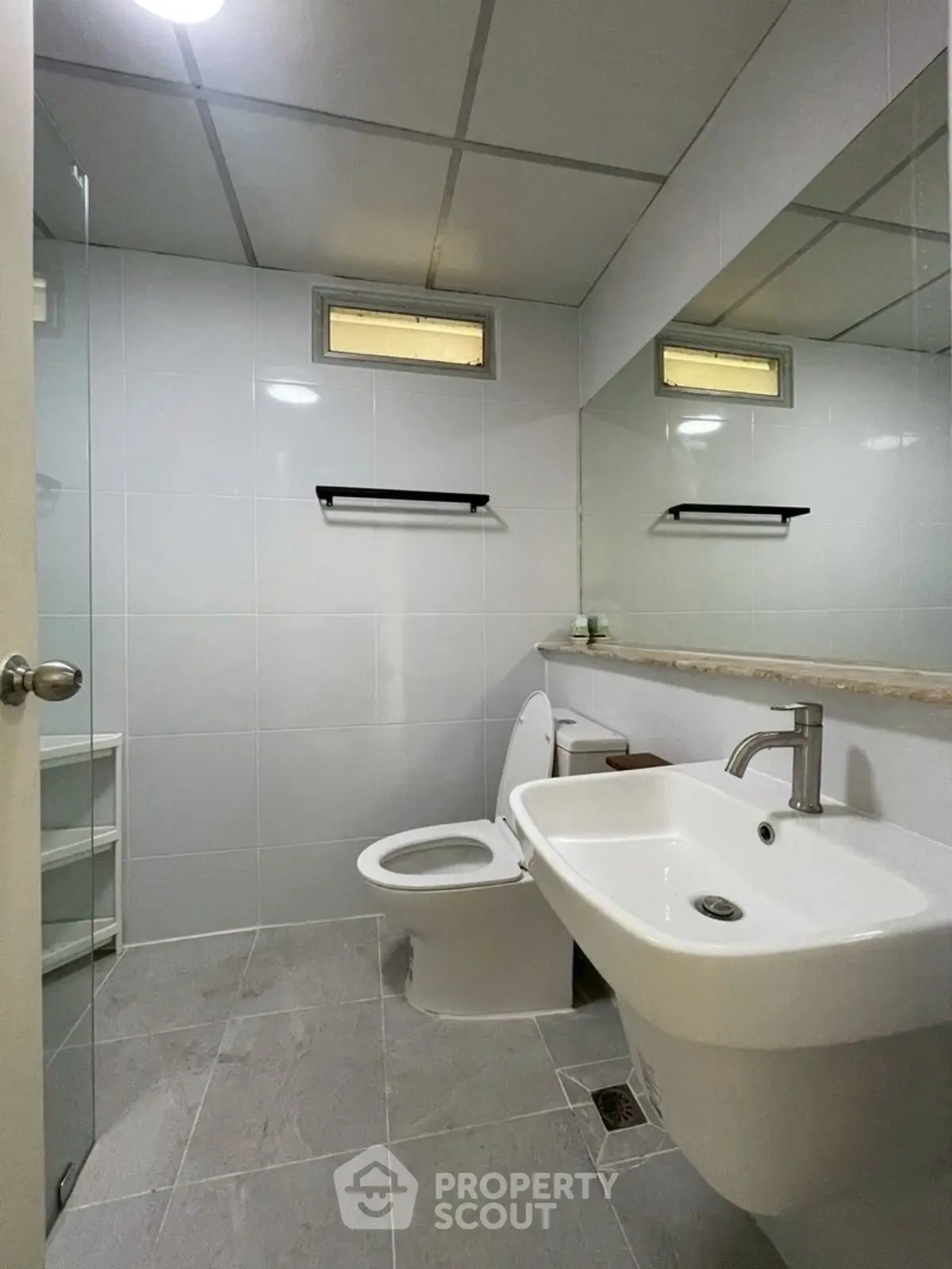 Modern bathroom with sleek fixtures and neutral tiles, featuring a spacious sink and toilet.