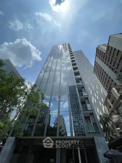 Stunning modern high-rise building with reflective glass facade and lush greenery in urban setting.