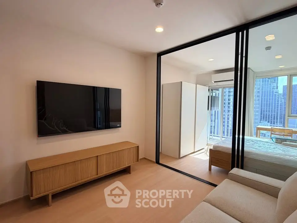 Modern living room with sleek TV and glass partition leading to a stylish bedroom with city view.