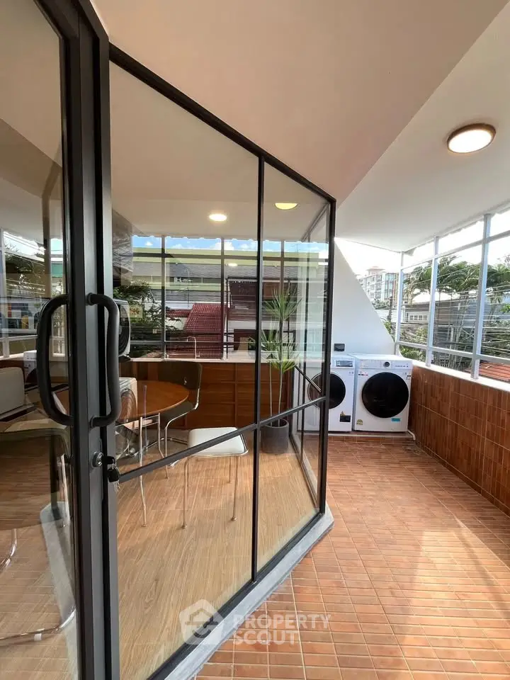 Modern balcony with glass doors, seating area, and laundry appliances.