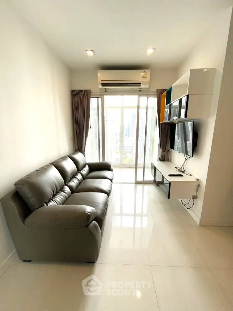 Modern living room with sleek leather sofa and wall-mounted TV, featuring a bright balcony view.
