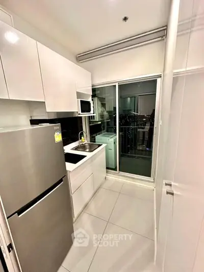 Modern kitchen with sleek white cabinets and stainless steel appliances, featuring a balcony view.