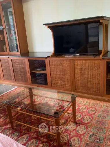 Cozy living room interior featuring a vintage wooden entertainment center with a modern flat-screen TV and a classic glass-top coffee table on an ornate rug.