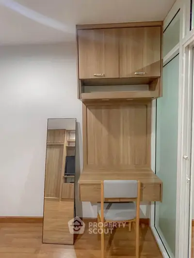 Modern study nook with wooden desk, chair, and mirror in a bright room.