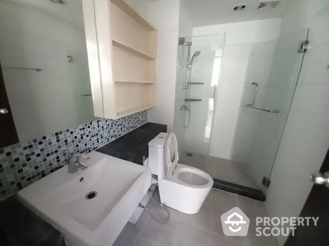 Modern bathroom with sleek design, featuring a glass shower enclosure, stylish tiling, and a well-lit vanity area for a refreshing ambiance.