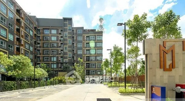 Modern apartment building with lush greenery and spacious parking area.