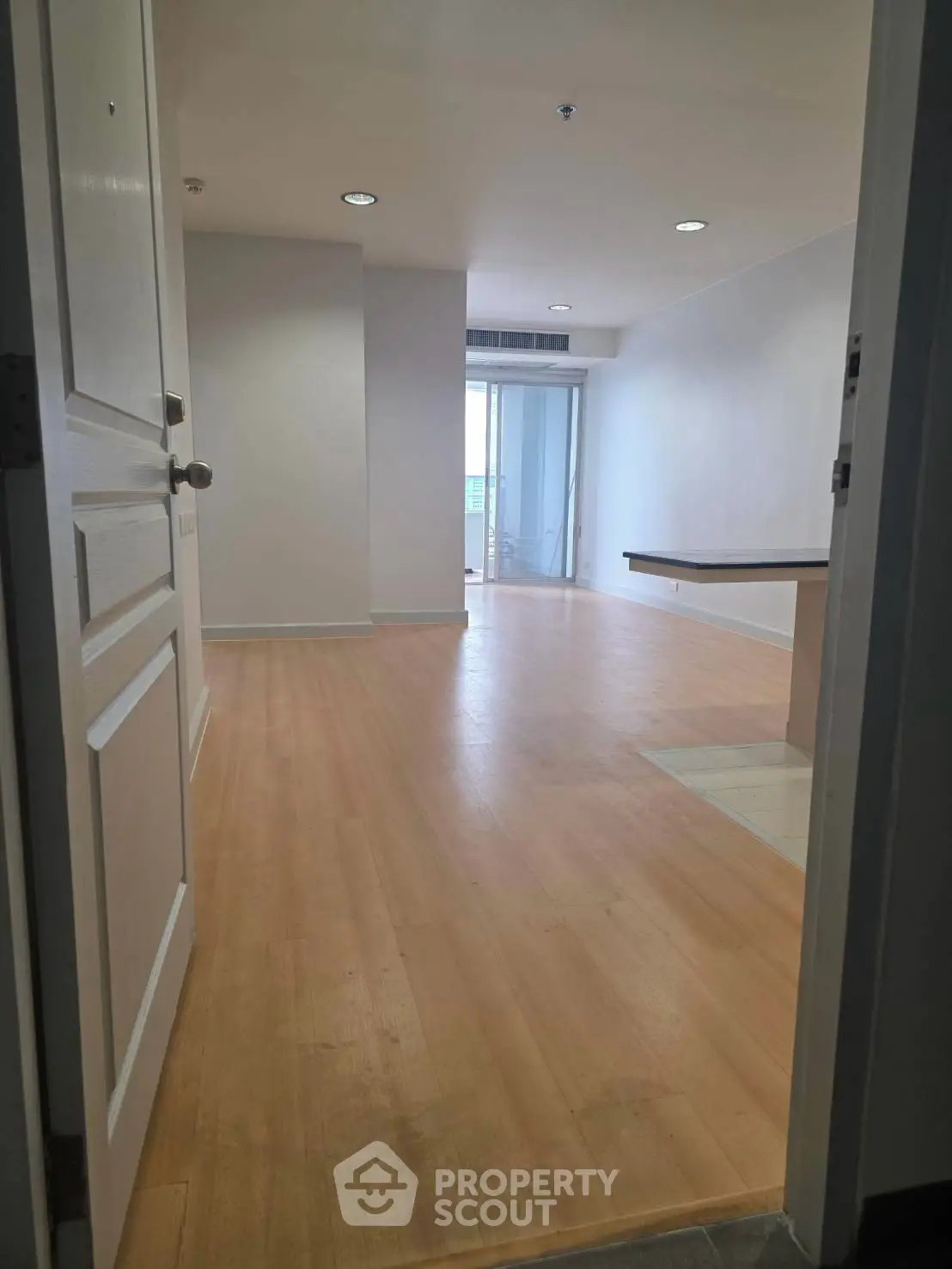 Spacious unfurnished living room with wooden flooring and balcony access in modern apartment.