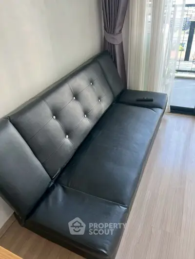 Modern living room with sleek black leather sofa and balcony view