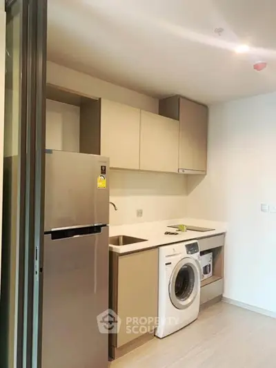 Modern kitchen with sleek cabinetry, fridge, and washing machine in compact layout.