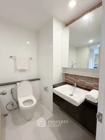 Modern bathroom with sleek fixtures and contemporary design, featuring a large mirror and elegant sink.