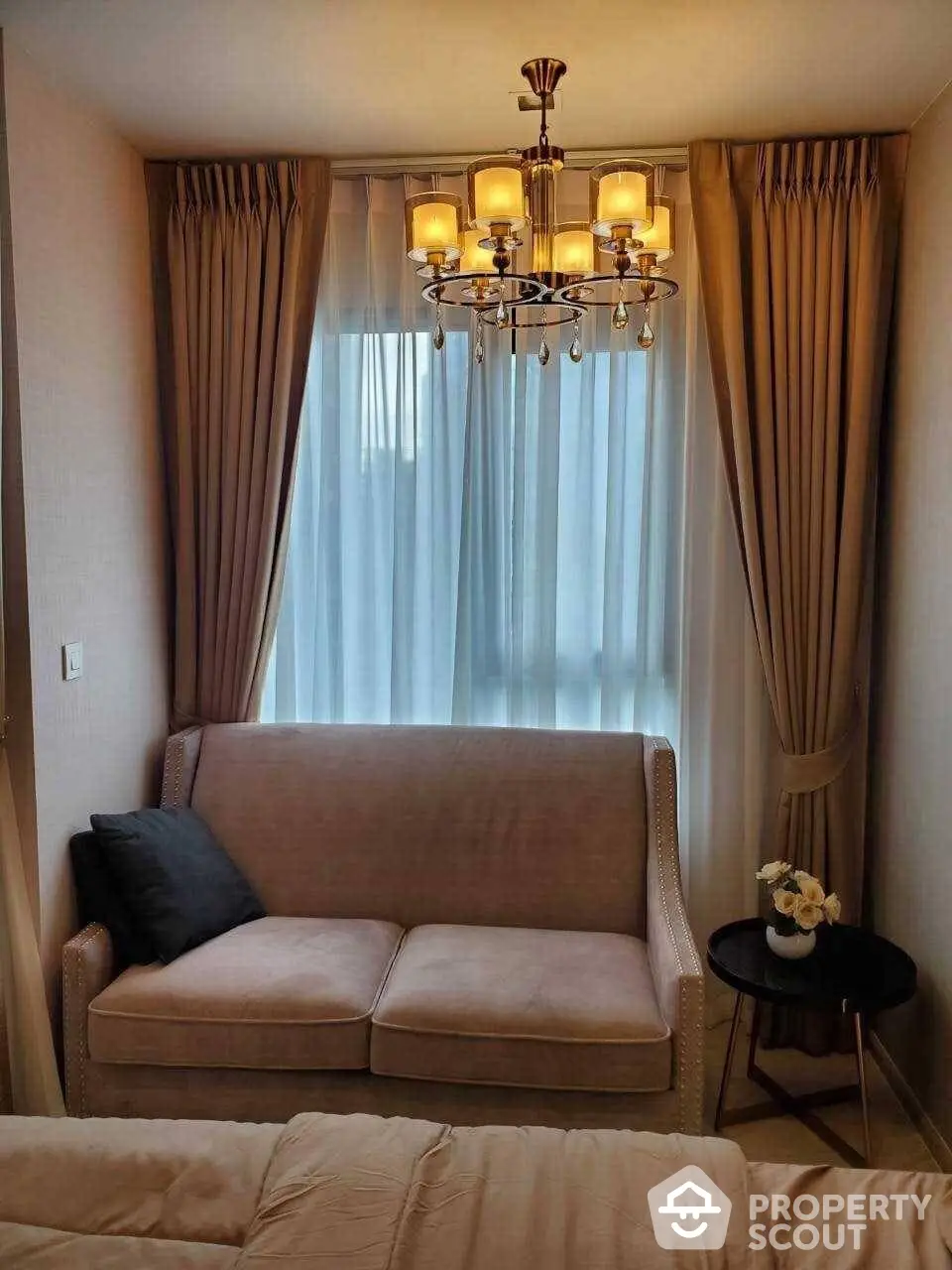 Elegant living room with plush sofa, sophisticated chandelier lighting, and sheer curtains creating a warm, inviting atmosphere perfect for relaxation or entertaining guests.