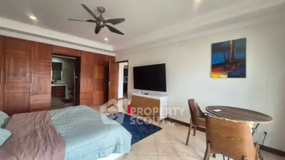 Spacious bedroom with modern decor, featuring a large TV, wooden furniture, and ceiling fan.