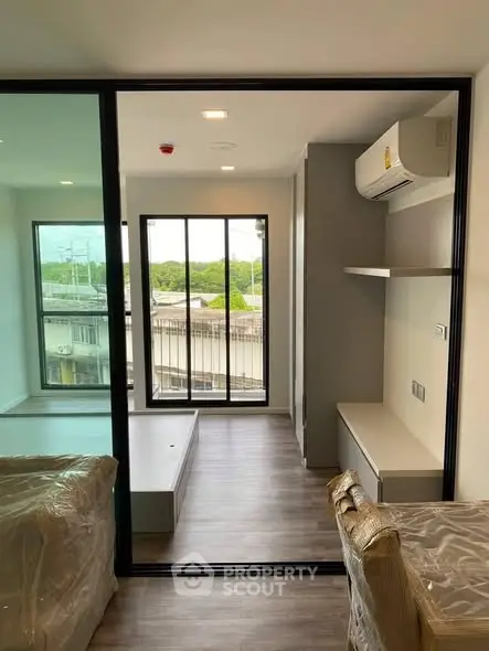 Modern apartment interior with large windows and balcony view, featuring sleek design and air conditioning.