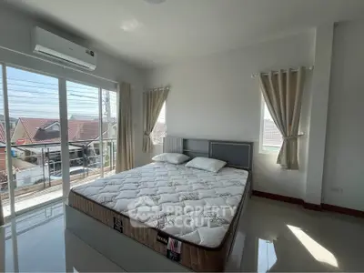 Bright bedroom with large windows and balcony access, featuring a comfortable bed and modern decor.