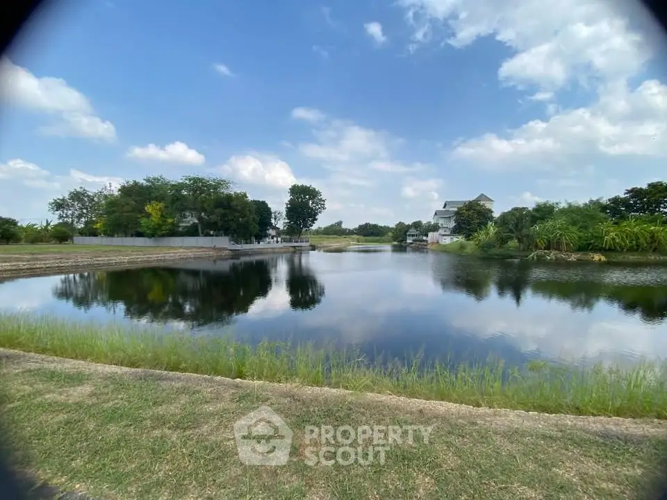 Scenic view of a serene pond with lush greenery and a distant house under a blue sky.