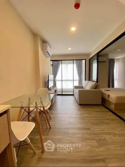 Modern living room with glass dining table and cozy sofa, featuring wooden flooring and natural light.