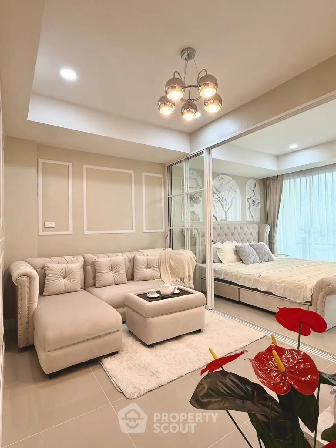 Elegant living room with plush sofa and modern lighting, adjacent to a cozy bedroom with natural light.