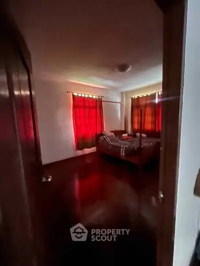 Cozy bedroom with red curtains and polished wooden floors, perfect for relaxation.