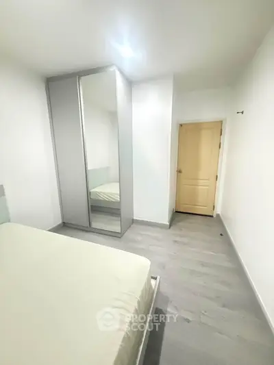 Modern minimalist bedroom with sleek mirrored wardrobe and light wood flooring.