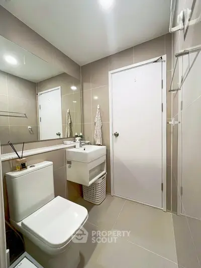 Modern bathroom with sleek fixtures and neutral tiles, featuring a compact sink and toilet.