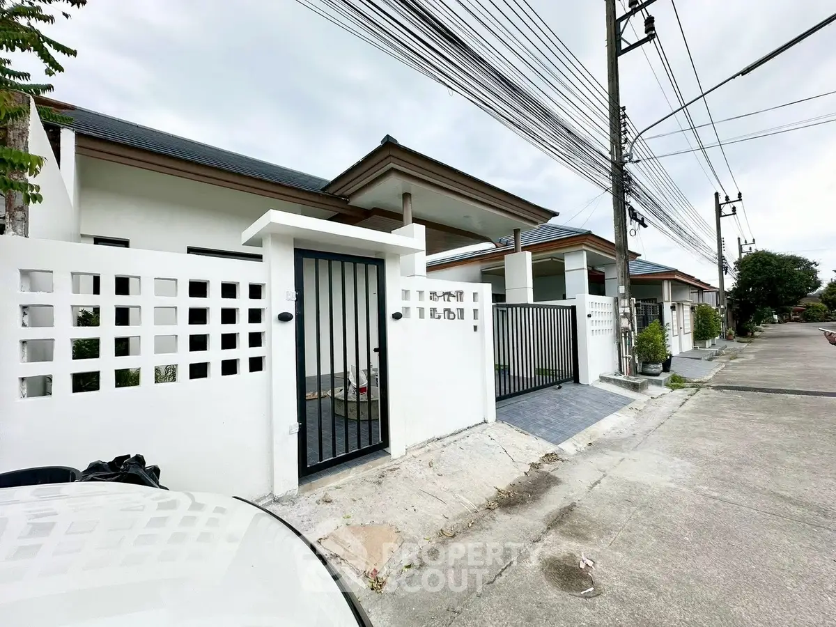Modern single-story house with gated entrance and paved driveway in suburban neighborhood.