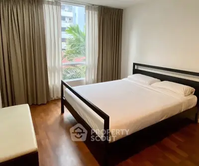 Spacious bedroom with large window and elegant wooden flooring in modern apartment.