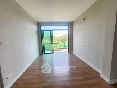 Spacious empty room with large window and wooden flooring, perfect for customization.