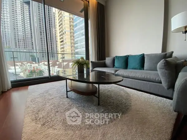 Modern living room with large windows and city view, featuring a stylish gray sofa and elegant coffee table.