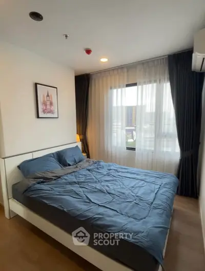 Cozy bedroom with modern decor and large window offering natural light.