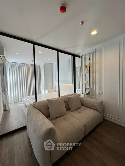 Modern bedroom with glass partition and cozy sofa, featuring elegant decor and natural light.