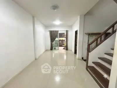 Spacious living room with modern staircase and large window for natural light.