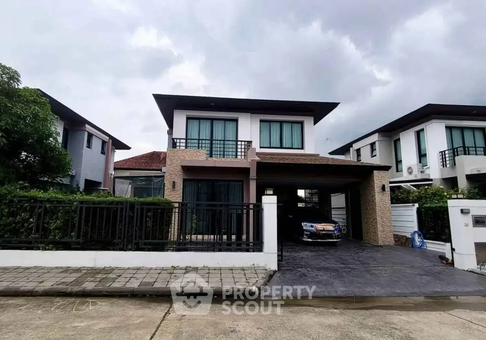 Modern two-story house with driveway and lush greenery under cloudy sky.