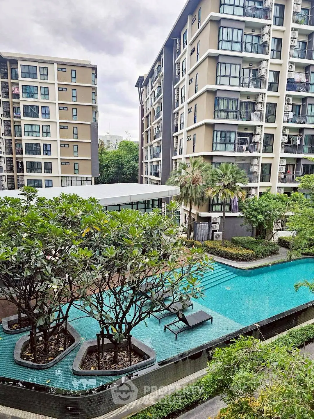 Modern apartment complex with lush greenery and inviting swimming pool.