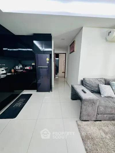 Modern open-layout kitchen and living room with sleek black appliances and cozy gray sofa.