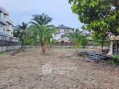 Vacant land with palm trees and residential building in the background, ideal for development.