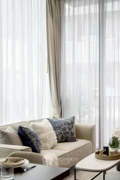 Elegant living room with plush sofa, stylish cushions, and sheer curtains for a cozy ambiance.