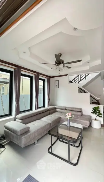 Modern living room with stylish gray sectional sofa, ceiling fan, and large windows for natural light.