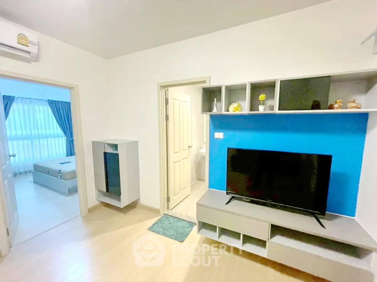 Modern living room with TV and stylish shelving, leading to a bright bedroom with natural light.
