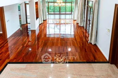 Spacious living room with polished wooden floors and large windows offering garden views.
