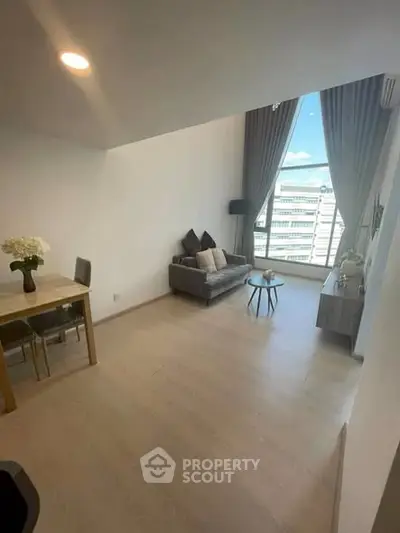 Spacious living room with high ceiling and large window offering city view, modern decor and natural light.