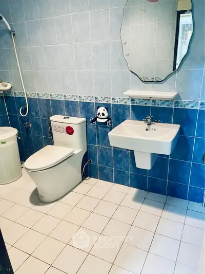 Spacious bathroom with modern fixtures and blue tile accents, featuring a sleek sink and toilet.