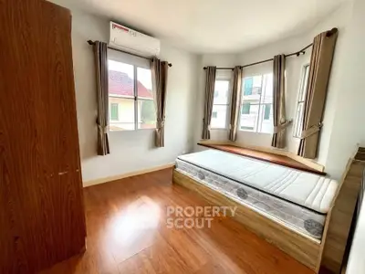 Bright bedroom with large windows and wooden flooring, featuring a built-in wardrobe and air conditioning.