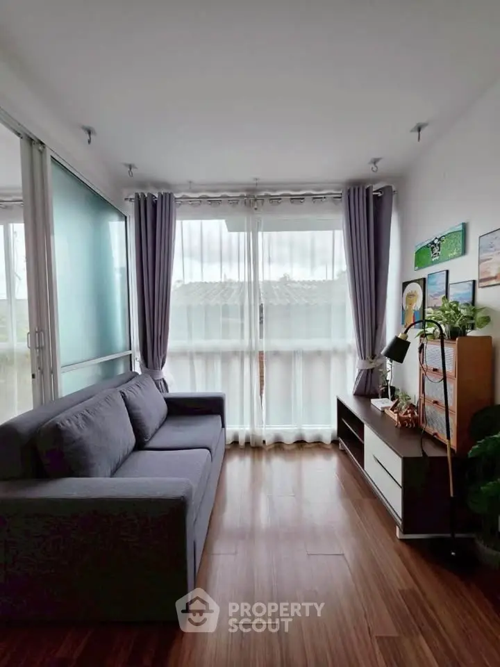 Charming living room with cozy sofa and natural light through large windows, perfect for relaxation.