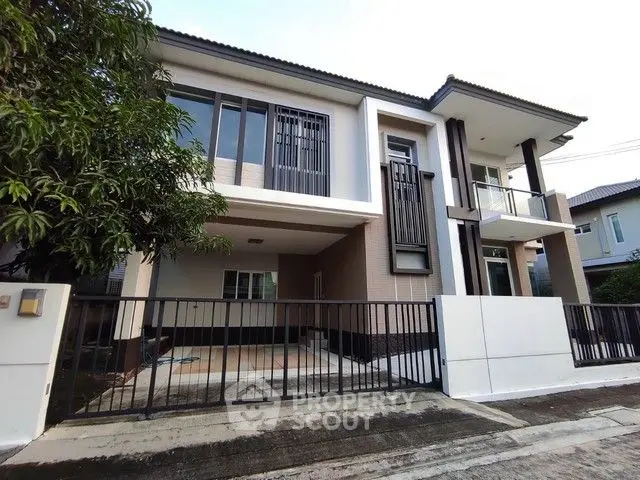 Modern two-story house with balcony and gated driveway in suburban neighborhood.