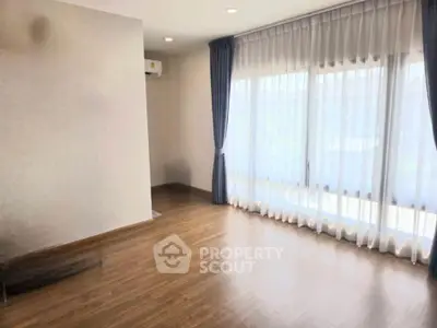 Spacious empty room with wooden flooring and large windows with curtains