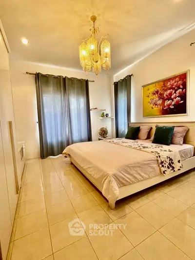Spacious bedroom with elegant decor and natural light, featuring a large bed and stylish chandelier.