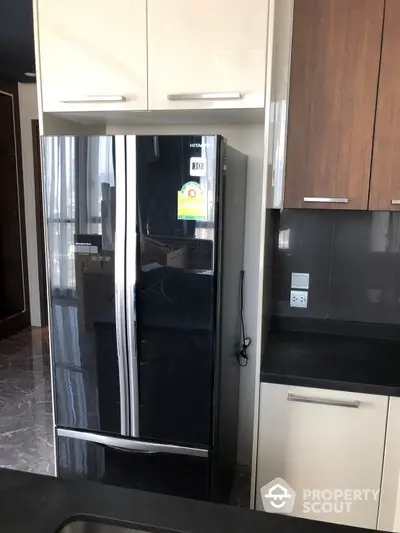 Sleek modern kitchen with high-end stainless steel refrigerator, contrasting dark countertops, and a mix of white and wood cabinetry, showcasing a stylish and functional space.