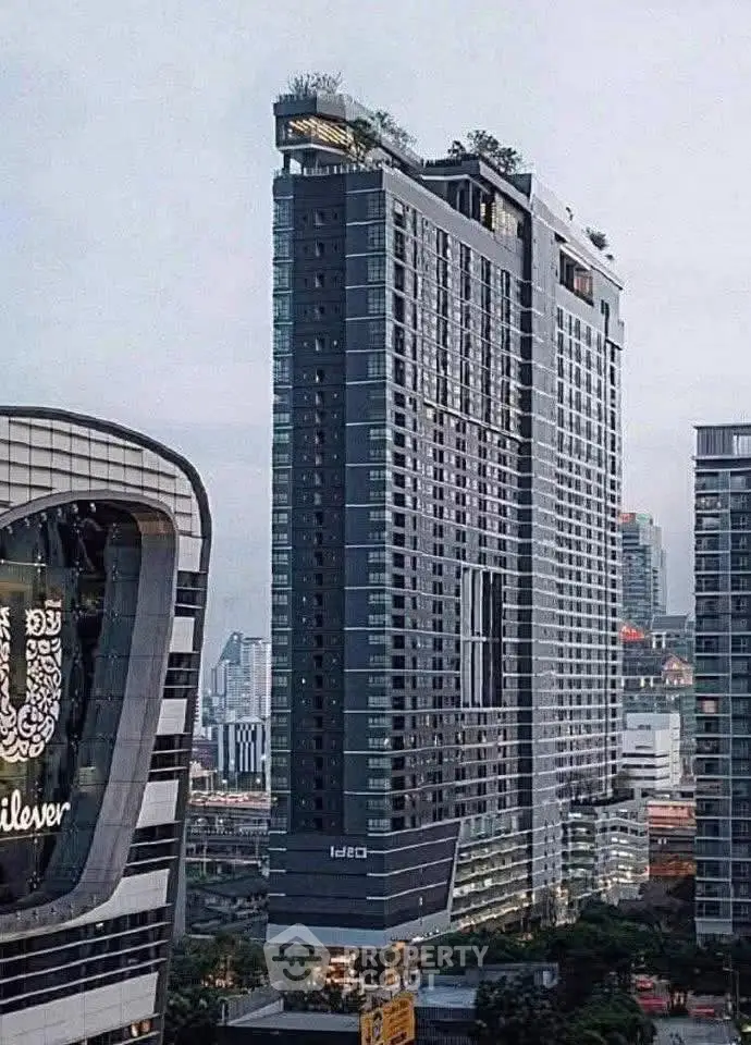 Modern high-rise building with sleek design and rooftop greenery in urban setting.